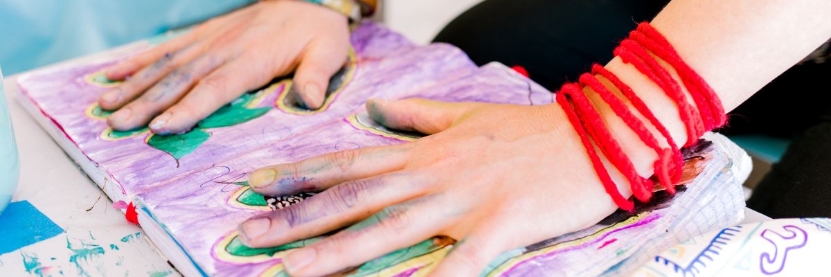 Image of paint splashed hands placed on an open art journal.